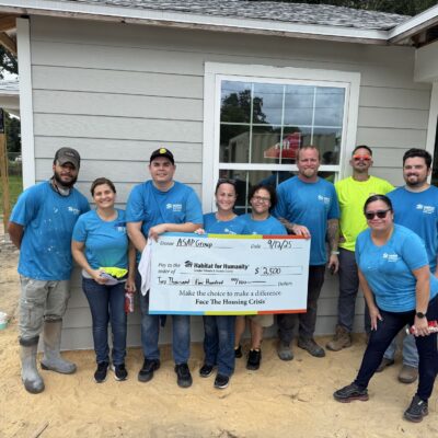 Nine people in blue hold a $2,350 Habitat for Humanity check.