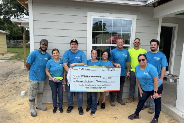 Nine people in blue hold a $2,350 Habitat for Humanity check.