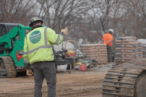 Worker in yellow jacket gesturing on active construction site.