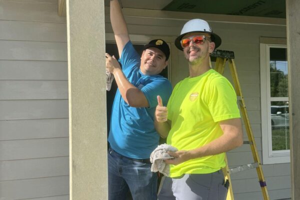 Two men work on house exterior; one gives a thumbs up.