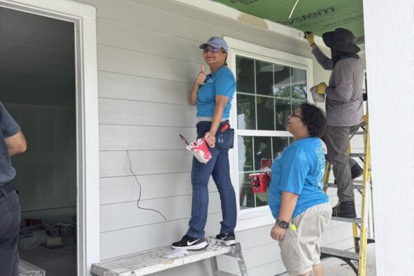 Four people work on a house exterior with tools and insulation.