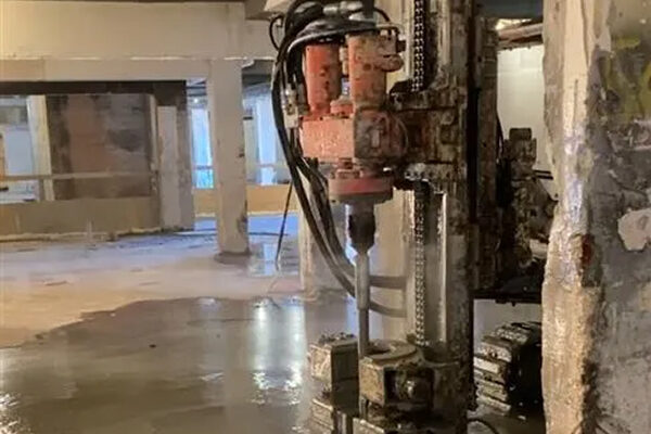 Industrial core drill stands upright on concrete in a damaged building.