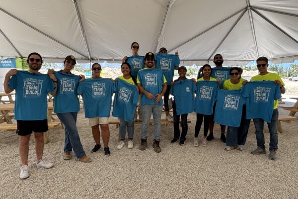 People under a tent hold blue Team Build T-shirts outside.