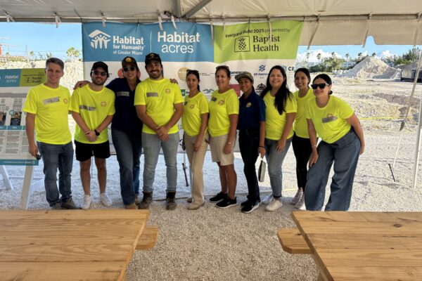 Group in yellow and blue shirts pose under tent at event.
