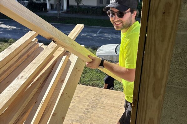 Man in neon green shirt carries wood up ramp at construction site.