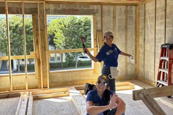 Two people work inside a wood-framed building; one waves.