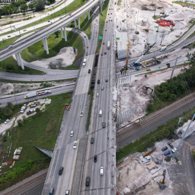 Aerial view of complex highway interchange with trains and construction.