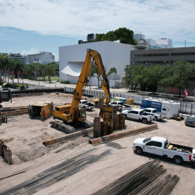 Construction site with machinery by white building and parking structure.