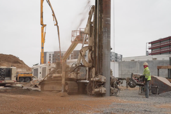 Workers drill into ground using heavy machinery at construction site.