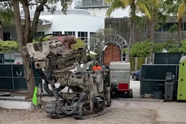 Tracked construction robot on gravel before modern building and palms.