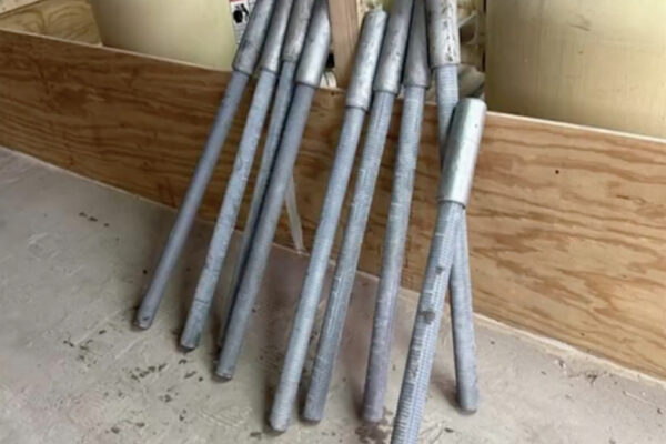 Eight metal anchor bolts lean against a wooden barrier.