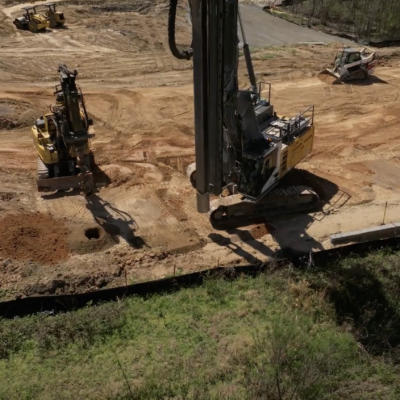 Construction site with machines drilling and workers on cleared earth.