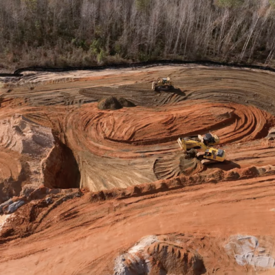 Aerial view of two excavators on reddish soil at construction site.