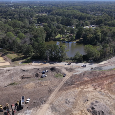 Aerial view: construction site, machinery, dirt roads, pond, trees.