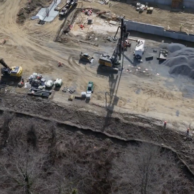 Aerial view: construction site, machinery, vehicles, dirt near woods.