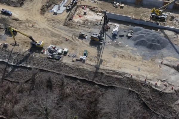 Aerial view: construction site, machinery, vehicles, dirt near woods.