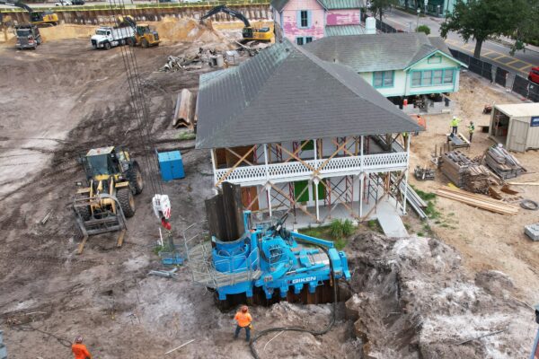Workers and heavy machinery at dug-up site near historic houses.