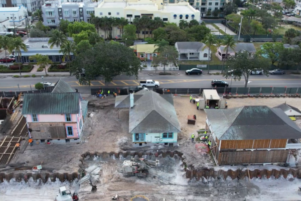 Aerial view: three houses under construction, road and cars nearby.