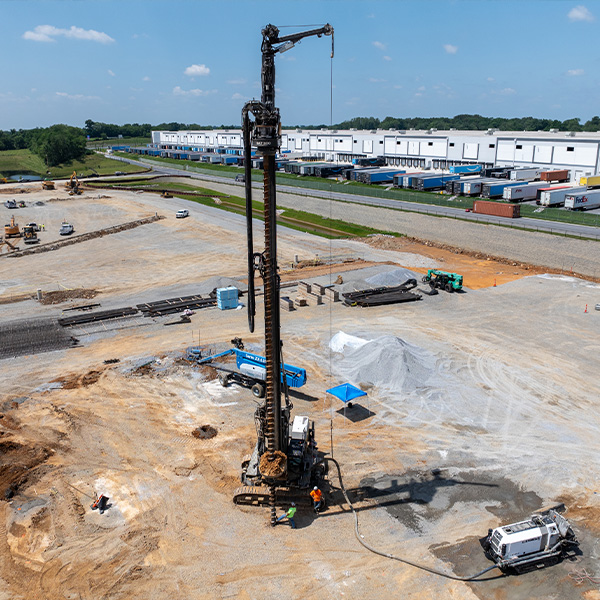 Drilling rig at construction site with workers and warehouses.