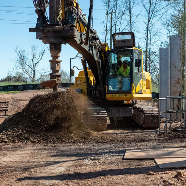 Worker uses yellow excavator, piling dirt at busy construction site.