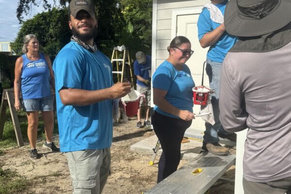 People in blue shirts painting a small building outside.