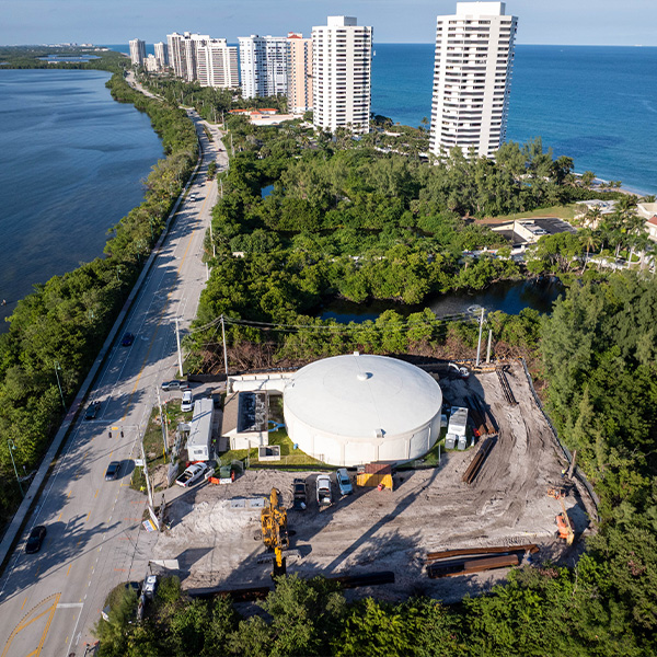 Aerial view: construction site with machinery by coastal circular structure.