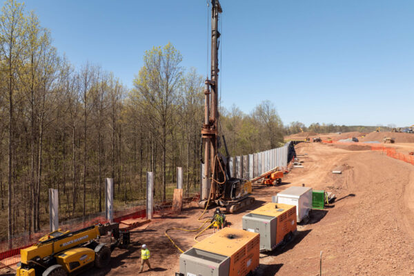 Workers operate heavy machinery and install concrete pillars near forest.