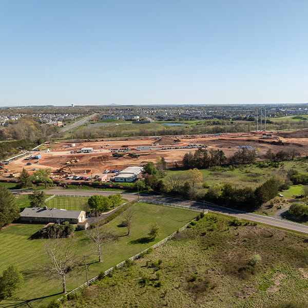 Aerial view of construction site amid green fields and trees.
