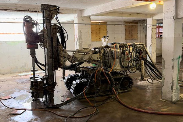 Drilling machine with tracks sits in a partly built building.