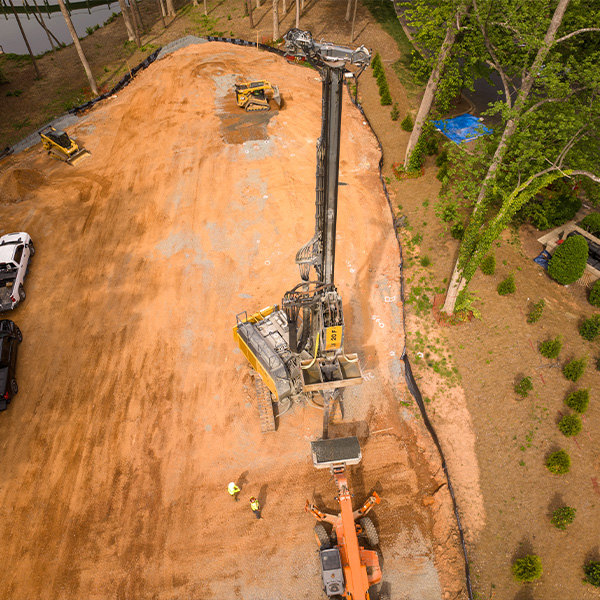 Aerial view: construction site, machinery, two workers, trees nearby.