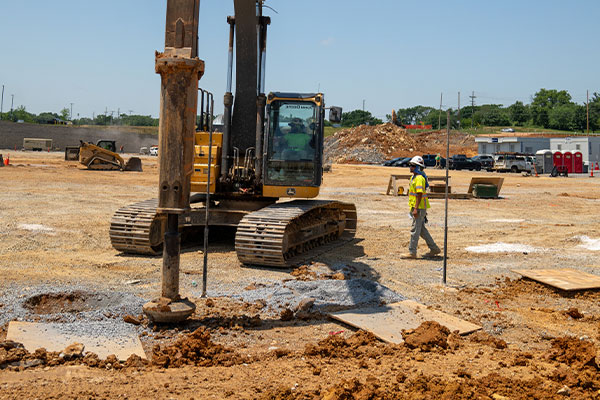 Worker walking by yellow excavator at dirt construction site.