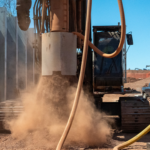 Construction drill stirring up dust on a sunny site.