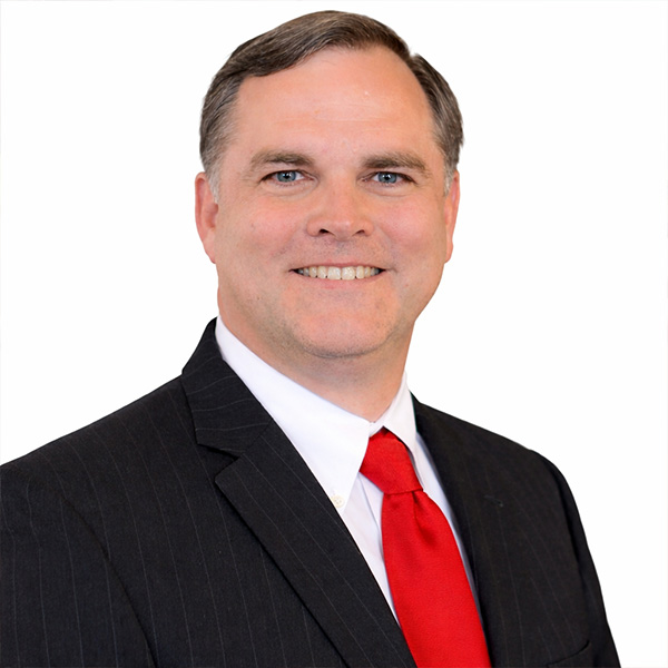 Man in pinstripe suit and red tie smiles at camera.