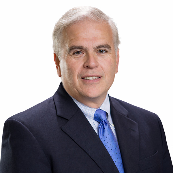 Gray-haired man in suit and blue tie on white background.