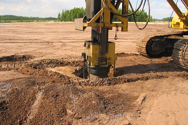 Drilling machine bores at construction site near cleared earth, forest.