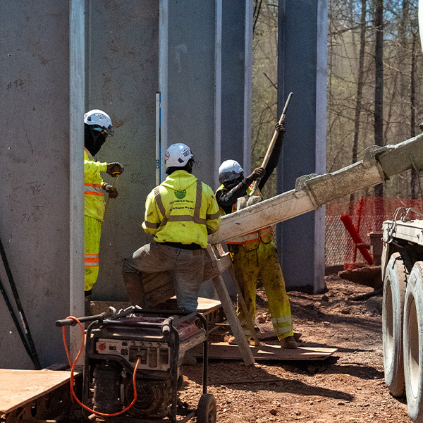 Three workers pour wet concrete into a foundation outdoors.