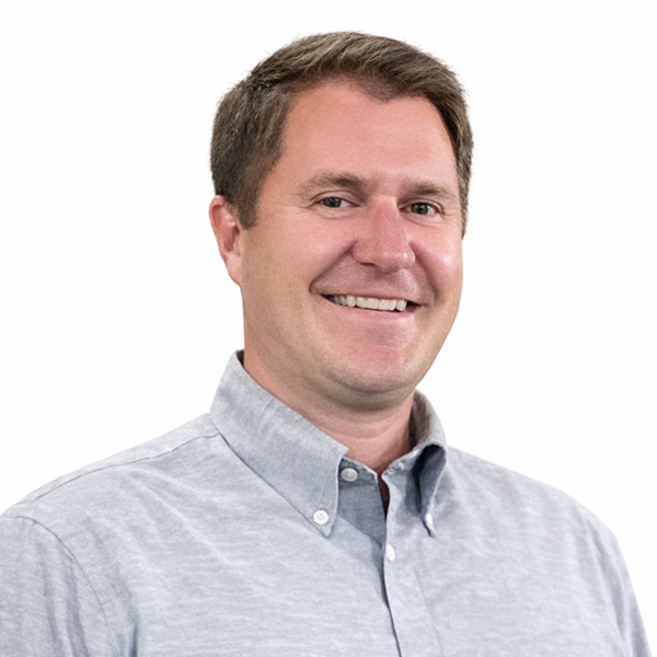 Man in gray shirt smiles at camera on white background.