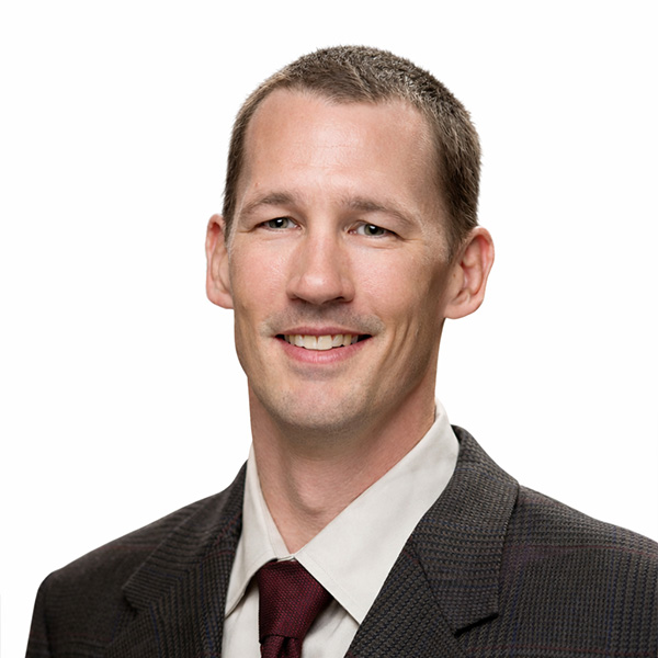 Smiling man in plaid jacket, red tie, white background.