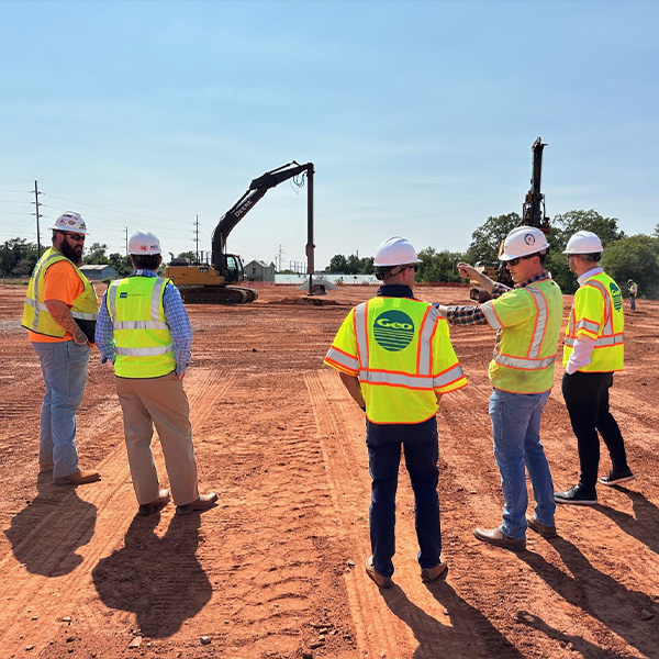 Five workers in safety vests and hard hats talk at construction site.
