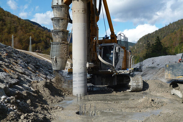 Drilling machine at construction site with rods and hills behind.