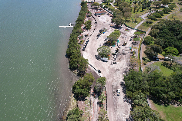 Aerial view: lakeshore construction, machinery, clear land, green park nearby.