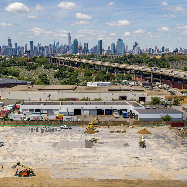 Construction site, machinery, industrial buildings, city skyline, highway.