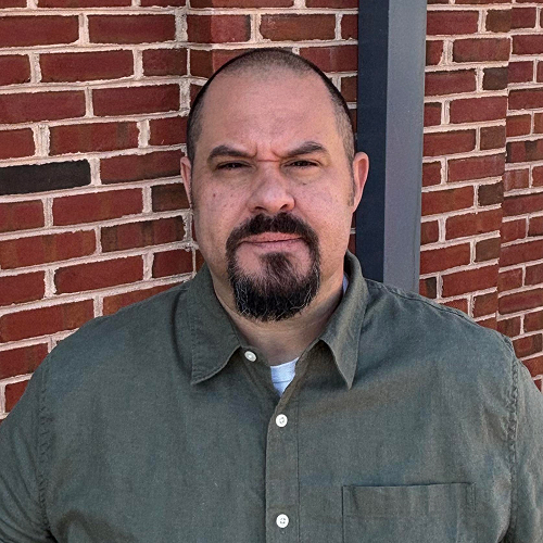man in a green shirt standing in front of a brick wall.