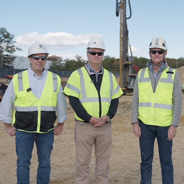Three men in safety gear stand at a construction site.